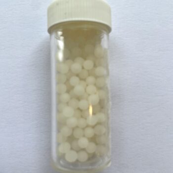 Large clear vial of white homeopathic pilules with white screw lid against a limewashed timber background