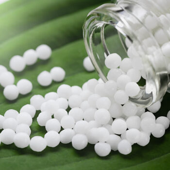 Homeopathic pills scattered from a bottle on a green leaf, close up